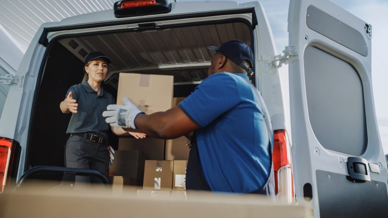 Logistics Warehouse Two Happy Diverse Workers Talk, Joke use Hand Pallet Truck Start Loading Delivery Truck with Cardboard Boxes, Online Orders, Purchases, E-Commerce Goods.