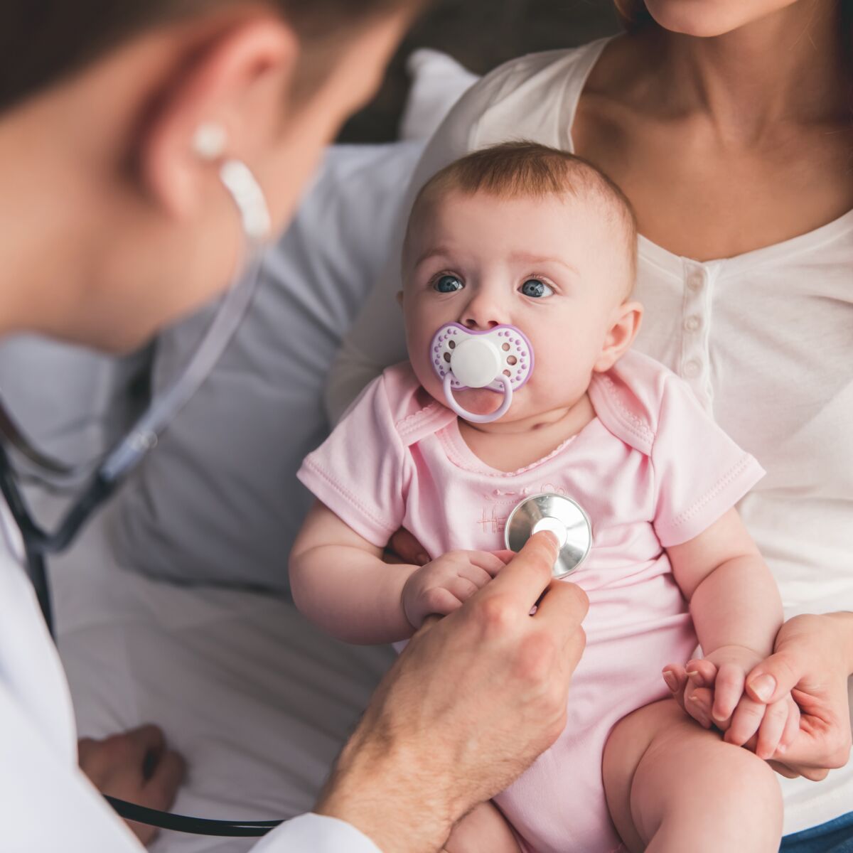 Beautiful young mom is holding her cute baby while doctor is listening to baby's lungs
